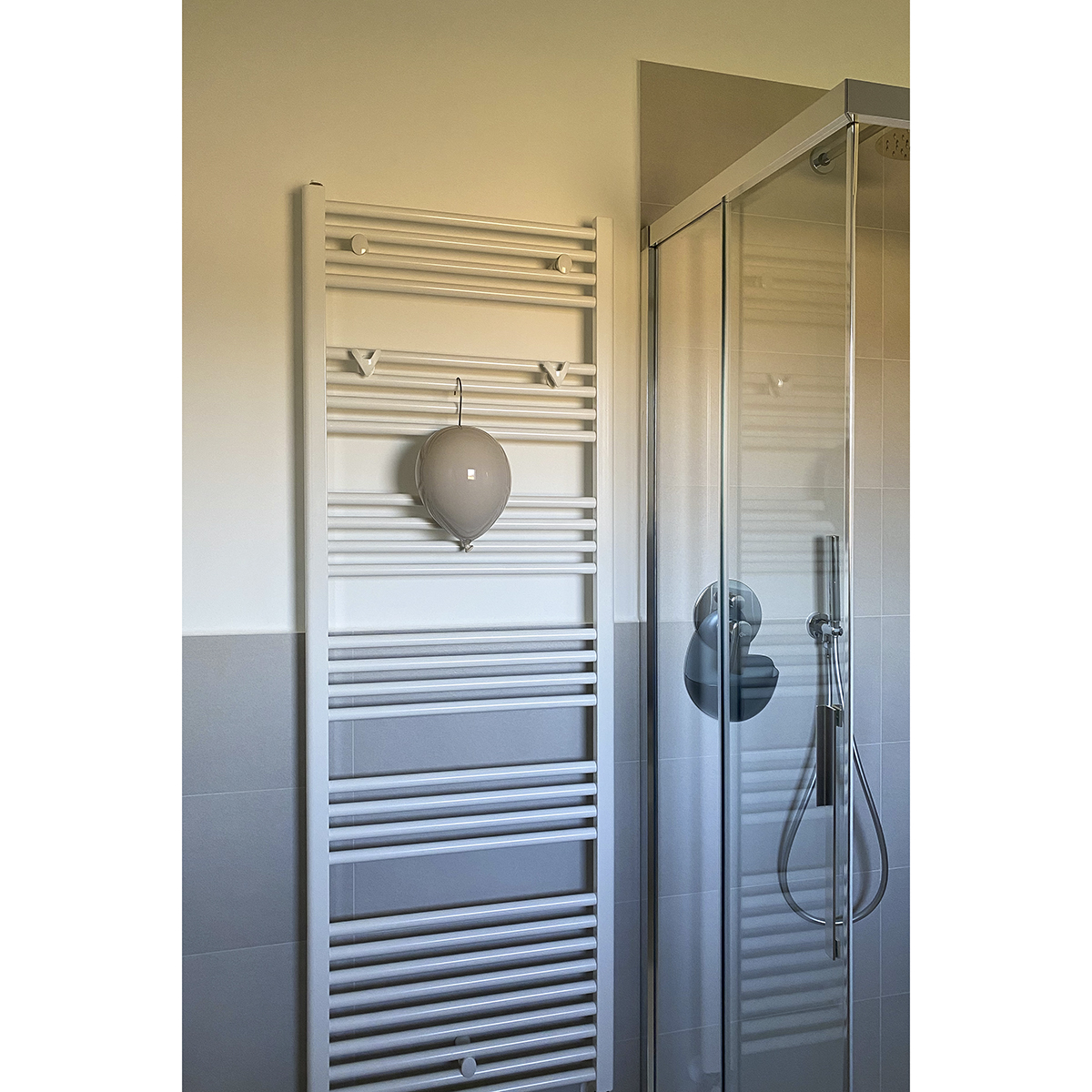 un radiatore bianco posto accanto ad un box doccia trasparente è decorato con un umidificatore design a forma di palloncino in ceramica grigia