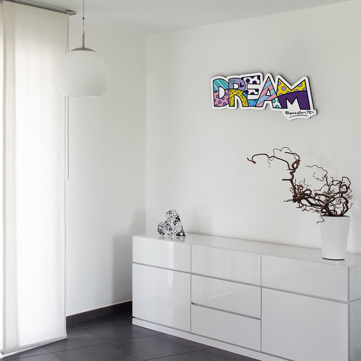 la scritta Dream a caratteri cubitali e decorata secondo lo stile pop fà risalto di sè su una parete bianca in un ambiente tutto bianco
