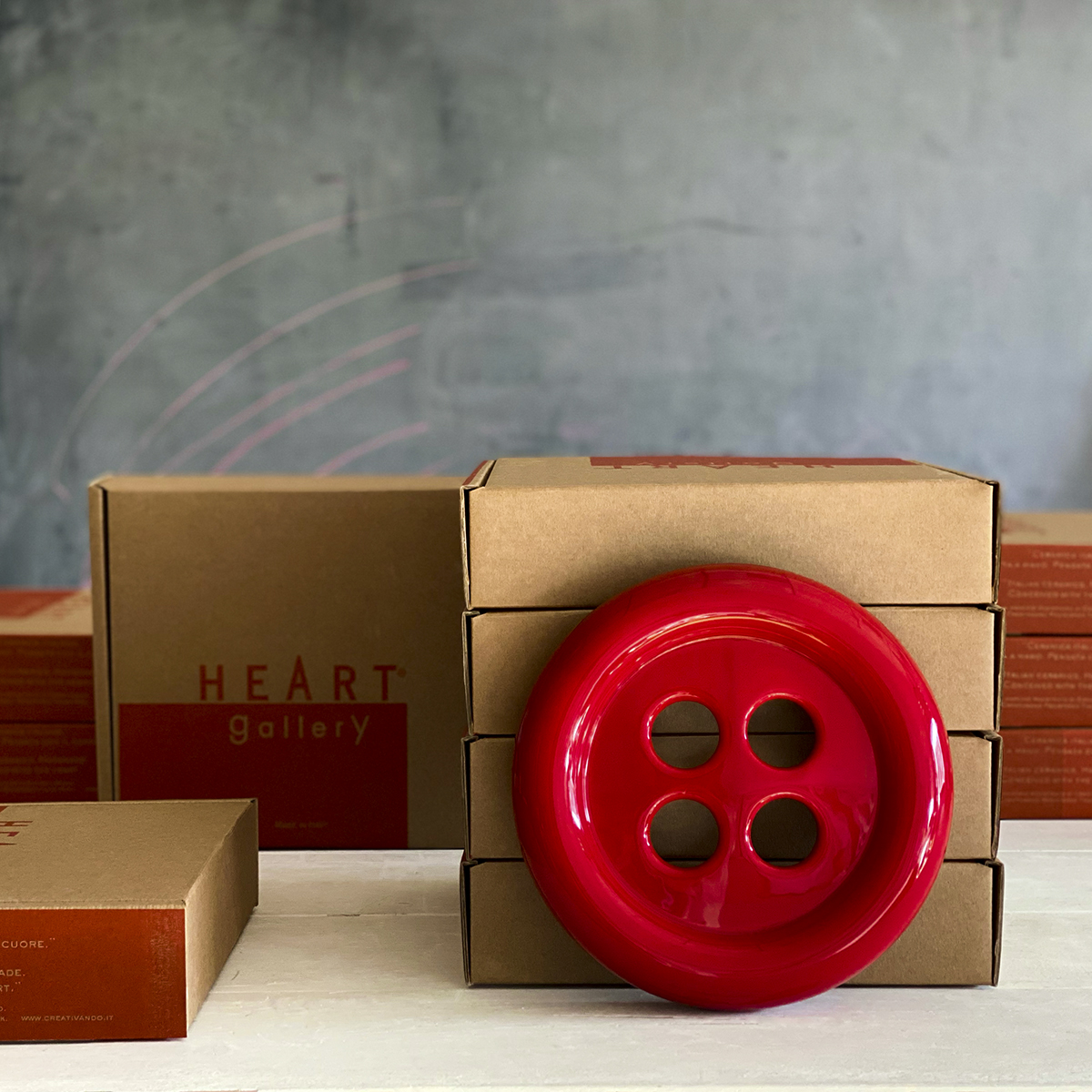 umidificatore in ceramica a forma di bottone rosso per radiatore è appoggiato sulle scatole della confezione.