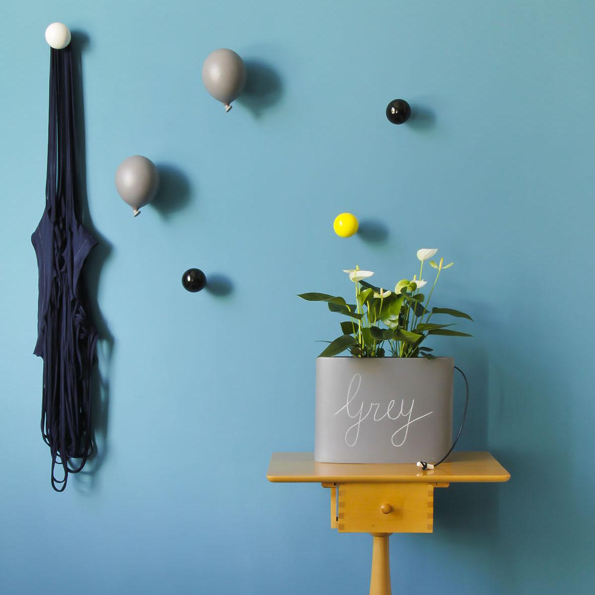 parete azzurra decorata con appendiabiti a forma di palloncino grigio e con diversi pomelli appendiabiti in ordine sparso