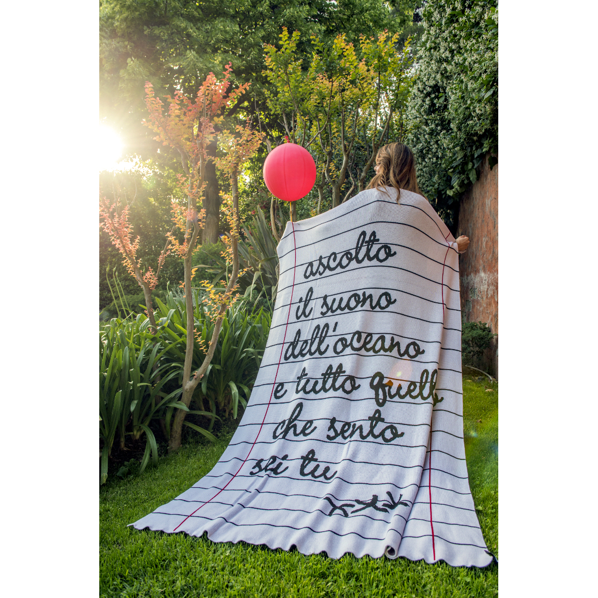 coperta in cotone con scritte usata come mantello da una ragazza in un giardino