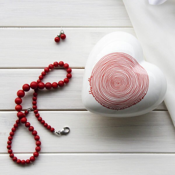 un cuore in ceramica bianco decorato con una spirale rossa ed una scritta è appoggiato