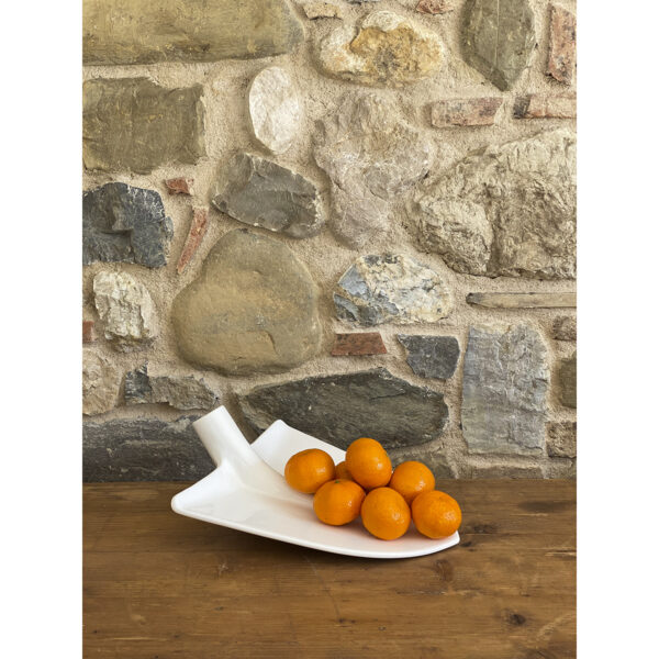 una pala in ceramica bianca funge da elemento decorativo e porta frutta su una tavola di legno in un ambiente rustico