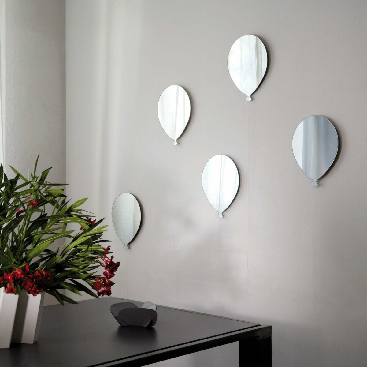 un bouquet di 5 palloncini in vetro formano una composizione di specchi su una parete bianca. I palloncini sono rifiniti anche con un filo bianco