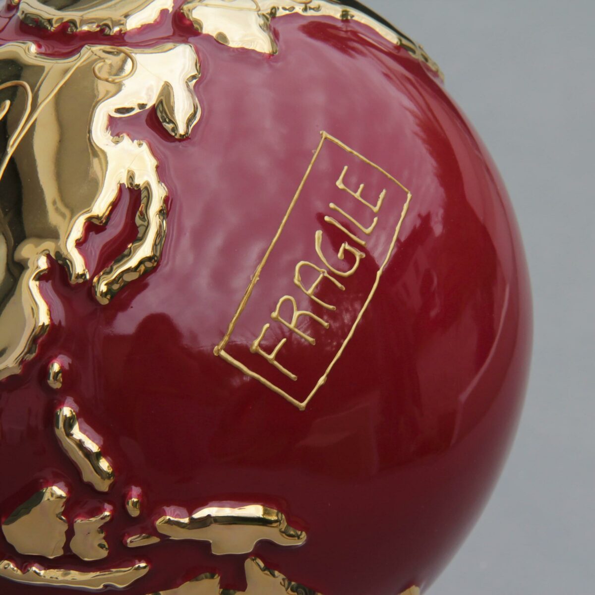 particolare globo in ceramica rosso rappresentante la terra con la scritta "Fragile" dorata