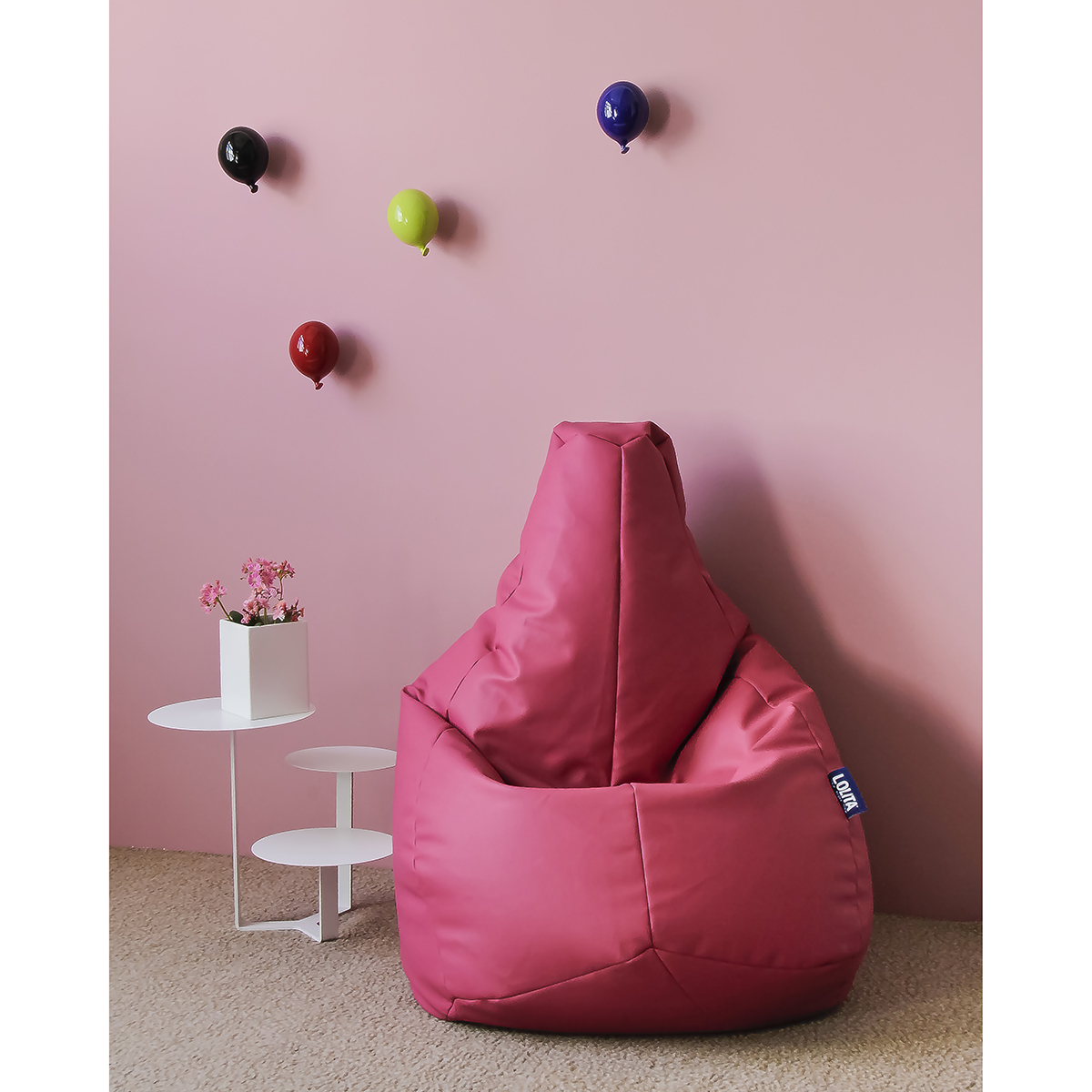poltrona a sacco in morbida ecopelle color rosa ortensia in un angolo di cameretta decorato con palloncini di ceramica a muro e tavolino a tre ripiani bianco