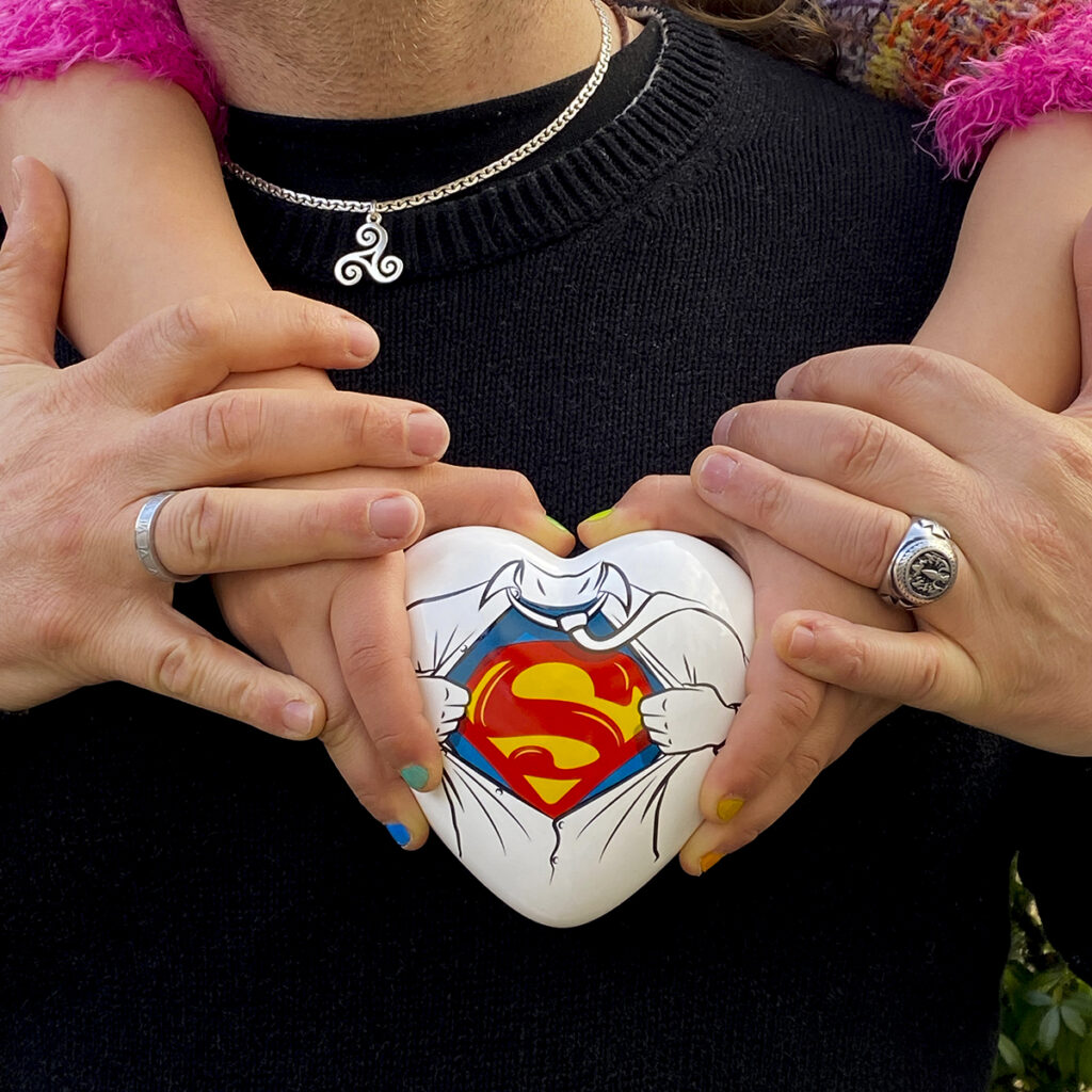 un cuore in ceramica bianco &egrave; tenuto nelle mani di una bambina, a sua volta nella mani del pap&agrave;. sul cuore c'&egrave; la scritta "S" di superman
