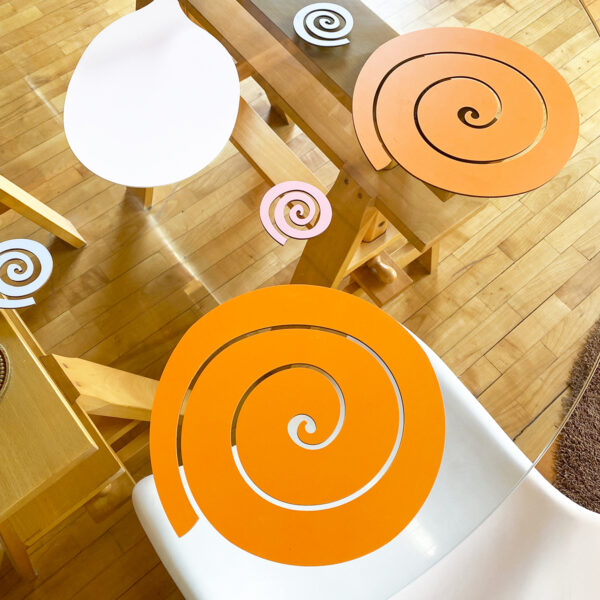 un tavolo in vetro rotondo è apparecchiato con delle spirali in legno arancione come sottopiatti