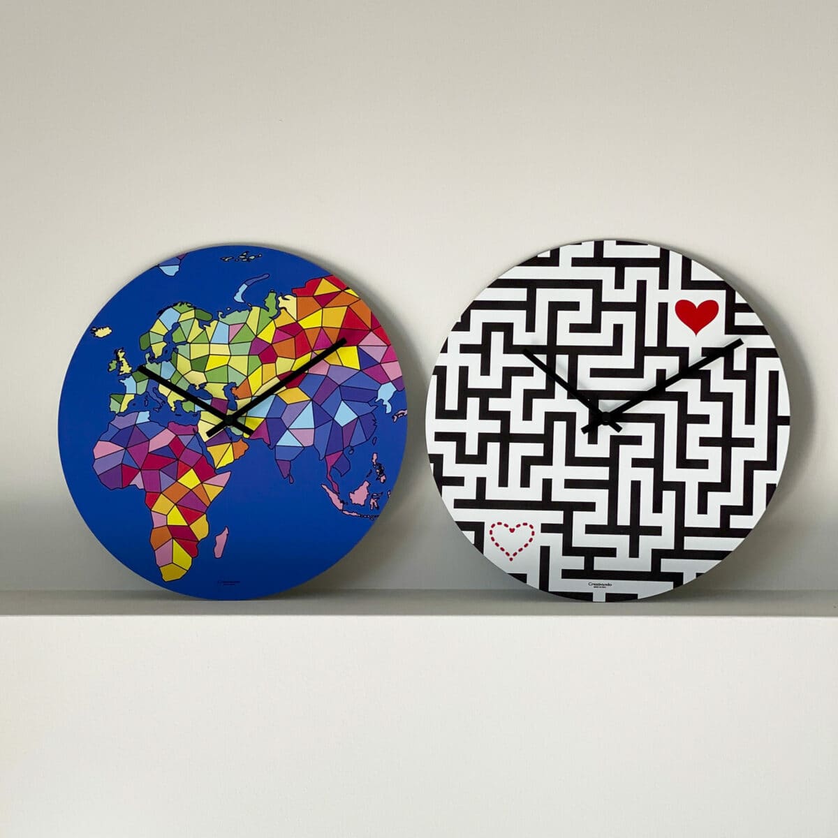 due orologi rotondi sono posti uno accanto all'altro: uno presenta un labirinto nero dove due cuoricini sono posti alle estremità mentre l'altro presenta una vista dell'eurasia e africa interpretata artisticamente.