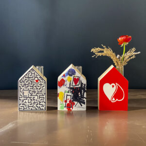 gruppo di tre casette minimal decorate artisticamente, una delle quali al posto del camino ha una provetta di vetro dalla quale esce un mazzetto di fiori