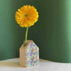 una casetta di legno decorata con tante margherite stampate ha una bella gerbera gialla che fuoriesce dal camino