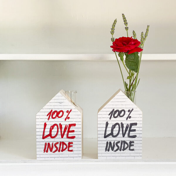 due casette in legno con la facciata decorata con la scritta 100% love inside, una nera ed una rossa, sono appoggiate su una mensola bianca