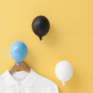 tra palloncini blu, bianco e nero, sono appesi ad un muro giallo e su quello blu è appesa una gruccia con una maglietta bianca